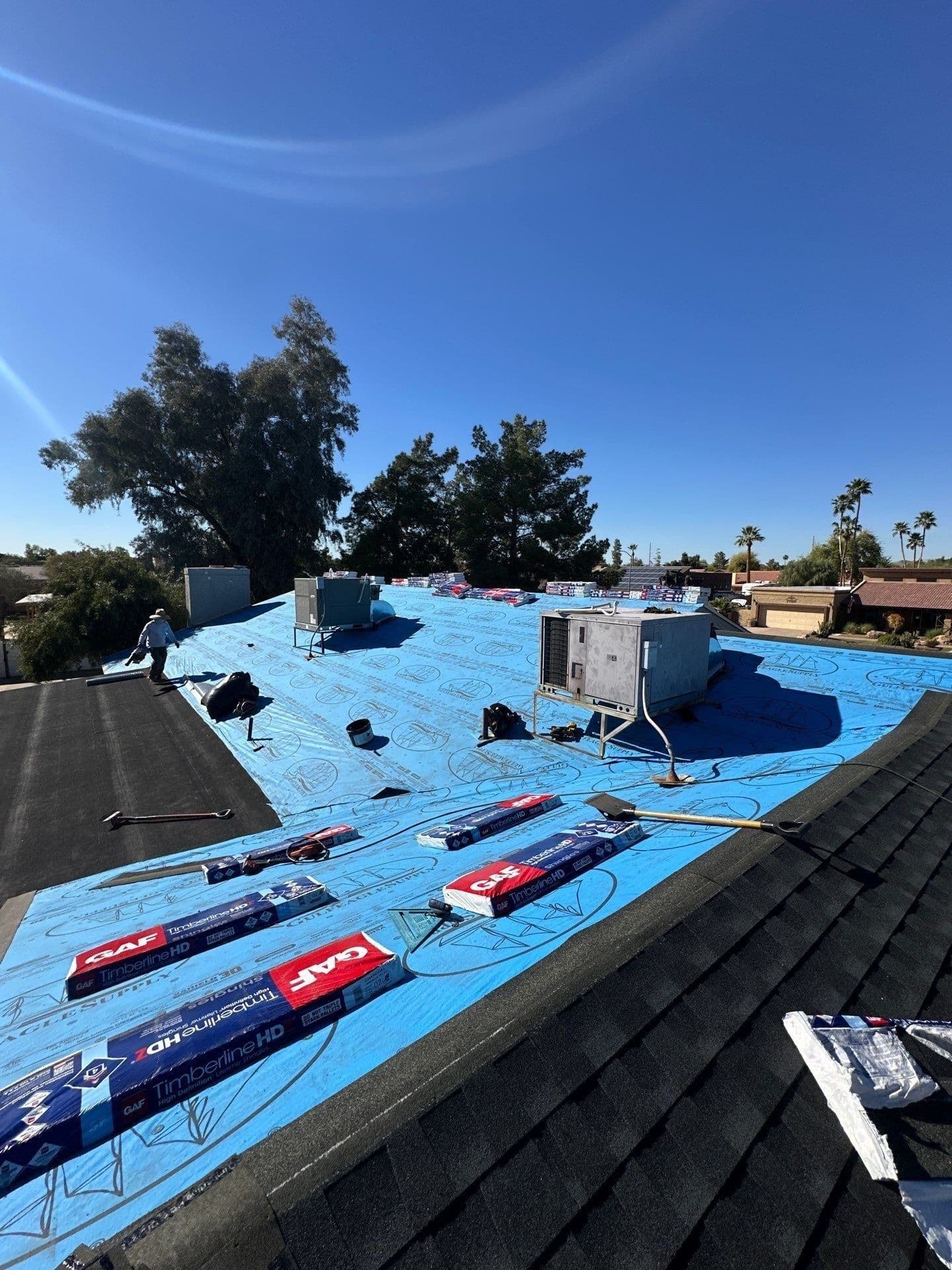 Asphalt shingle reroof in progress in Glendale, AZ with blue synthetic underlayment and GAF shingle bundles staged